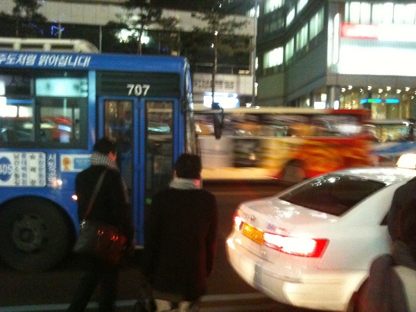 사람들은 차도를 하나 넘어 가야 버스를 탈 수있다.